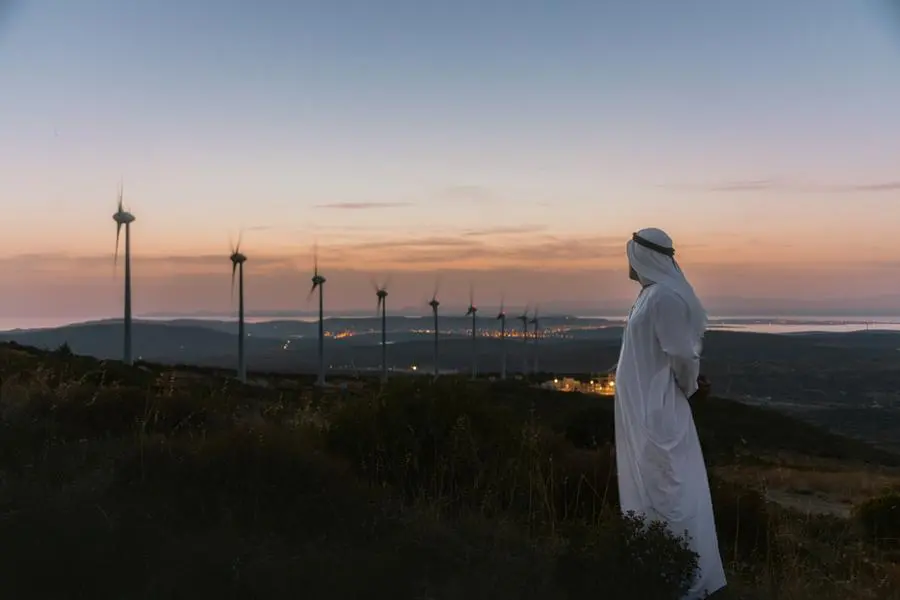 Arab Sheikh with traditional Emirati clothes looking for the energy industry and standing beside a wind turbines farm power station at sunset time. Image used for illustrative purpose. Getty Images , Getty Images