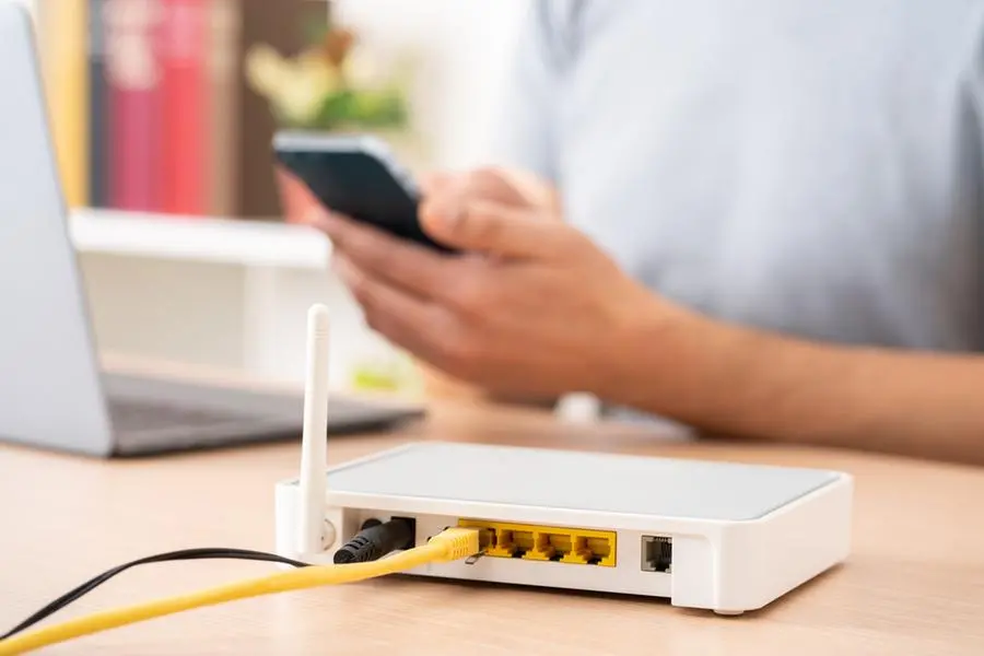 Close up of man hands using multiple devices with broadband router on foreground. Image used for illustrative purpose. Image courtesy: Getty Images/ Cunaplus_M.Faba
