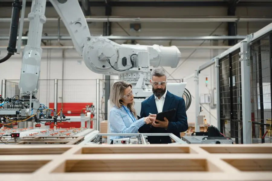 Female engineer and male project manager standing in modern industrial factory, talking about production of wooden furniture. Big furniture manufacturing facility with robotics, robotic arms and automation. Image used for illustrative purpose. Image courtesy: Getty Images/ HalfPoint , Getty Images