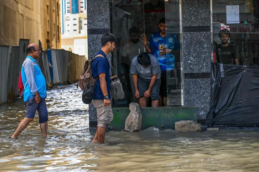 People wade through a flooded street following heavy rains in Sharjah on April 17, 2024. Dubai, the Middle East's financial centre, has been paralysed by the torrential rain that caused floods across the UAE and Bahrain and left 18 dead in Oman on April 14 and 15. (Photo by Ahmed RAMAZAN / AFP)
