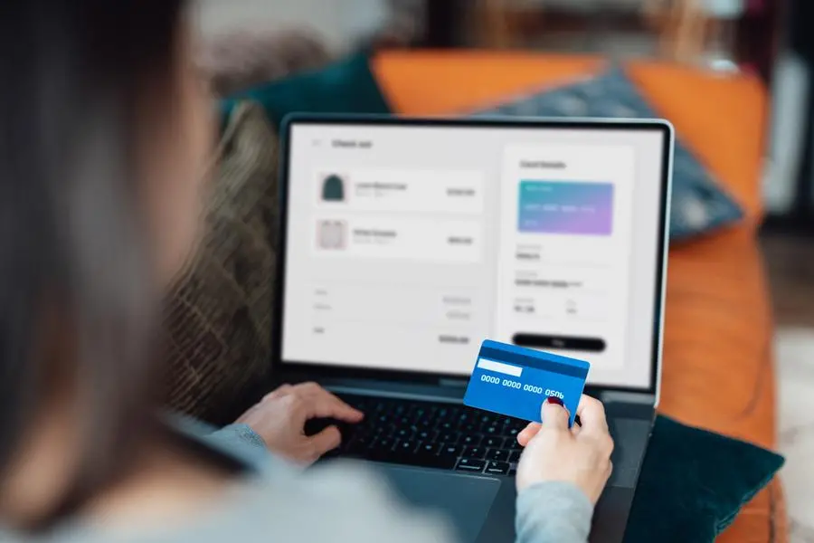 Above the shoulder view of a woman shopping clothes online on laptop, making payment with credit card. Enjoying seasonal sales. Image used for illustrative purpose Getty Images , Getty Images