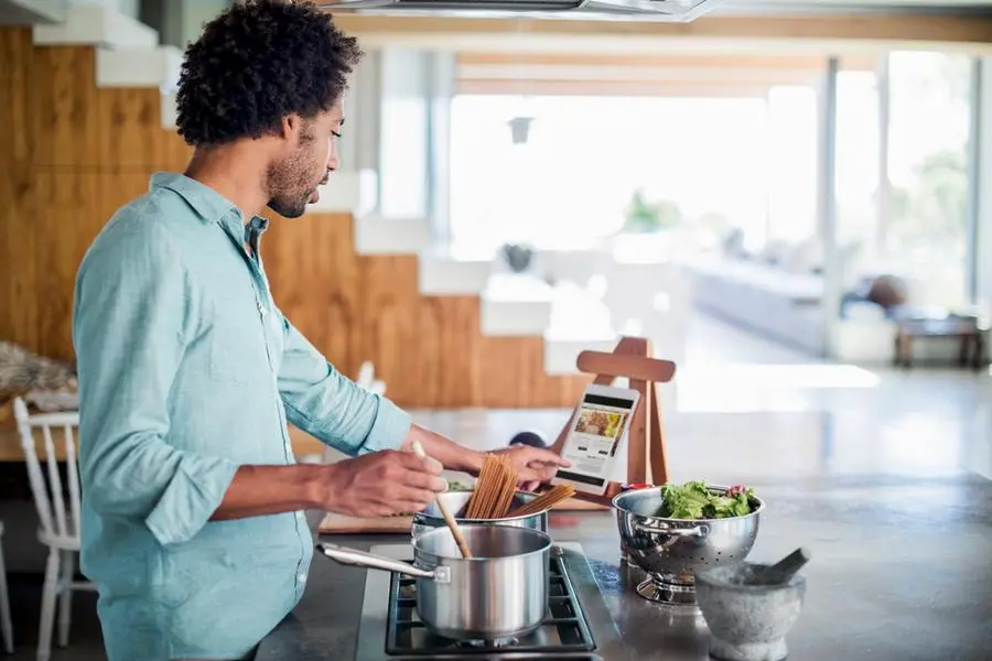 Man cooking in the kitchen while reading a recipe of a digital tablet. Image Courtesy: Getty Images , Getty Images/Getty Images