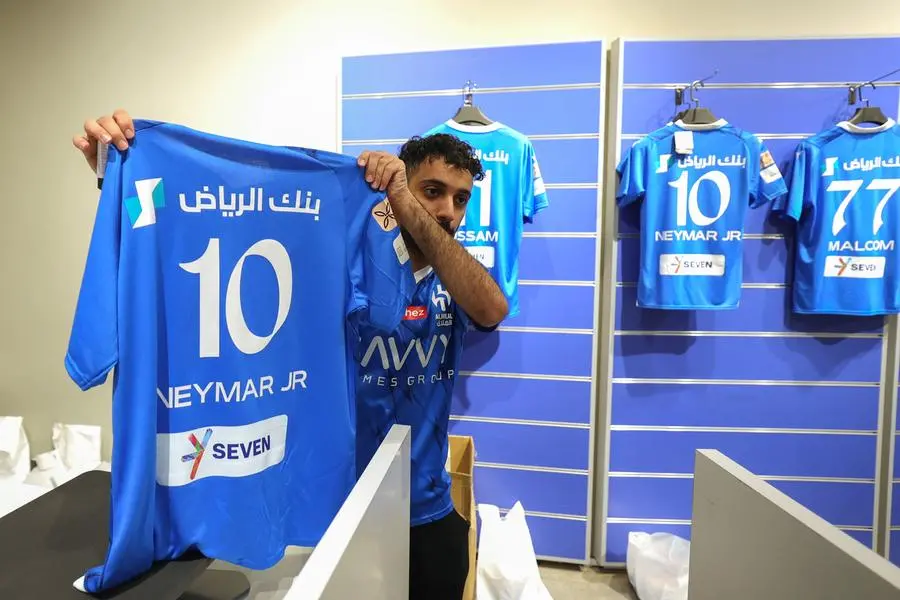 An employee of the Saudi Al-Hilal football club official shop displays a freshly-printed T-shirt bearing the name and number of Brazilian forward Neymar Jr. in Riyadh on August 15, 2023. Brazil forward Neymar has signed for Saudi Arabia's Al-Hilal from Paris Saint-Germain, the clubs announced today, joining Cristiano Ronaldo and Karim Benzema as the latest big name lured to the oil-rich Gulf state. (Photo by Fayez Nureldine / AFP)