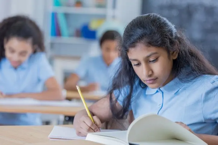 Indian middle schoolgirl works on class assignment at school. She is wearing a school uniform. She is looking at something in a book. , Getty Images/Getty Images