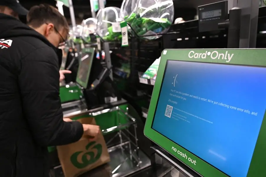 A customer takes care of his shopping next to blue screen at self-checkout terminals of a supermarket in Sydney on July 19, 2024. - A large-scale outage wrought havoc on IT systems across Australia, with the country's national broadcaster, its largest international airport and a major telecommunications company reporting issues. (Photo by Saeed KHAN / AFP)