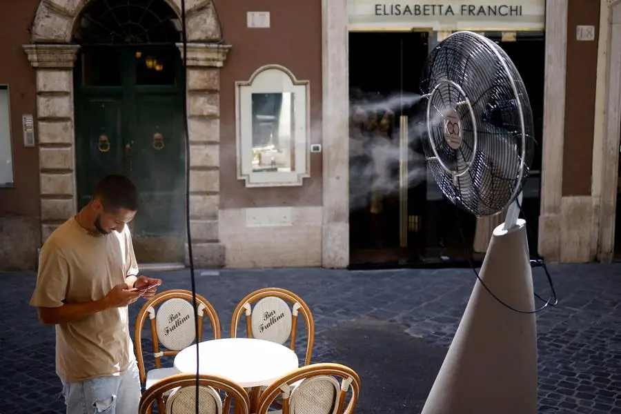 FILE PHOTO: A man checks his phone as he stands near a fan to cool off during a heatwave across Italy, in Rome, July 14, 2023. REUTERS/Guglielmo Mangiapane/File Photo , Reuters