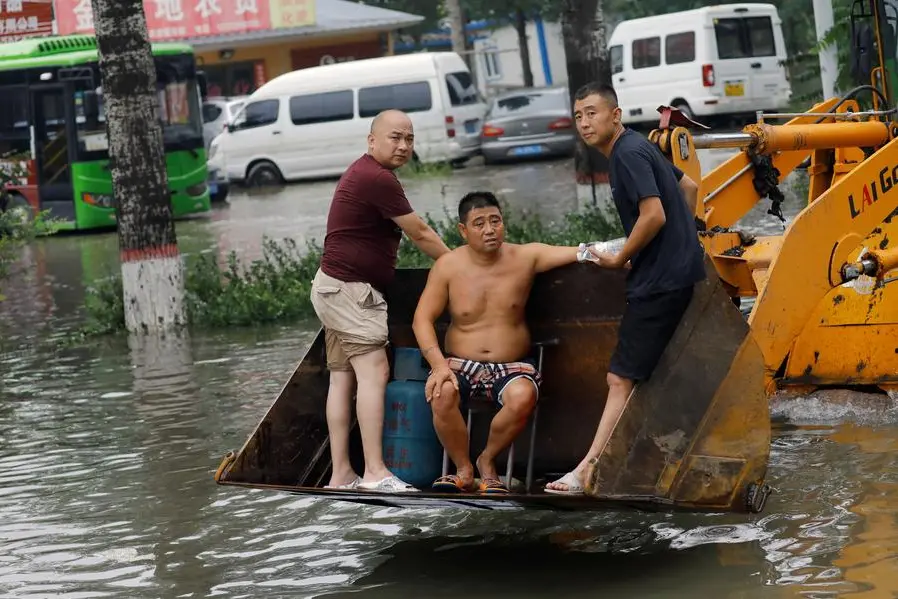 People stand on a front loader travelling through floodwaters after the rains and floods brought by remnants of Typhoon Doksuri, in Zhuozhou, Hebei province, China August 3, 2023. REUTERS/Tingshu Wang , Reuters/REUTERS