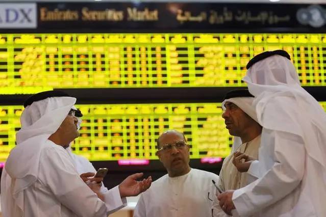 Investors speak in front of a screen displaying stock information at the Abu Dhabi Securities Exchange, June 25, 2014. Stringer, Reuters. Image used for illustrative purpose only.