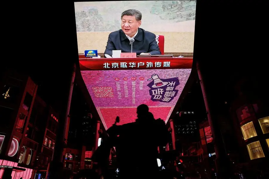 FILE PHOTO: A man rides a scooter past a giant screen showing news footage of Chinese President Xi Jinping attending a Chinese Communist Party politburo meeting, in Beijing, China December 9, 2024. REUTERS/Tingshu Wang. , Reuters