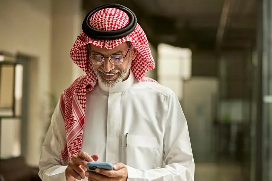 Waist-up front view of bearded Middle Eastern man in late 40s wearing traditional attire and showing positive emotion while looking at portable device. Image used for illustrative purpose. Getty Images , Getty Images