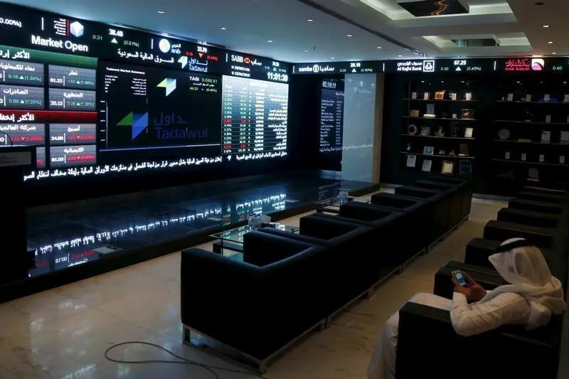 A trader uses his mobile as he monitors screens displaying stock information at the Saudi Stock Exchange (Tadawul) in Riyadh June 15, 2015.Faisal Al Nasser