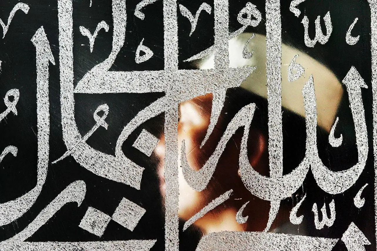 A Malaysian Muslim recites a prayer next to an Islamic calligraphy saying \"Allah\",  November 1, 2005. , Reuters Images/Bazuki Muhammad   