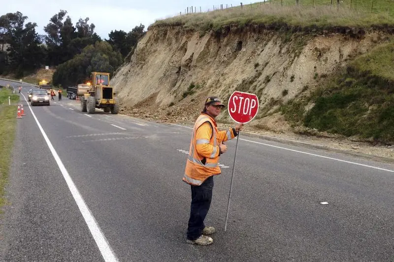 A man holds a traffic sign as workmen clear rubble from a road after the side of a hill collapsed following an earthquake on the outskirts of the town of Seddon in the Marlborough region, on New Zealand\\'s South Island August 16, 2013.REUTERS/Anthony Phelps  , Reuters Images/Anthony Phelps 
