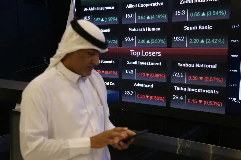 A man checks his mobile phone next to a screen with Saudi Stock Exchange (Tadawul) prices in Riyadh, Saudi Arabia September 16, 2019. REUTERS/Stringer
