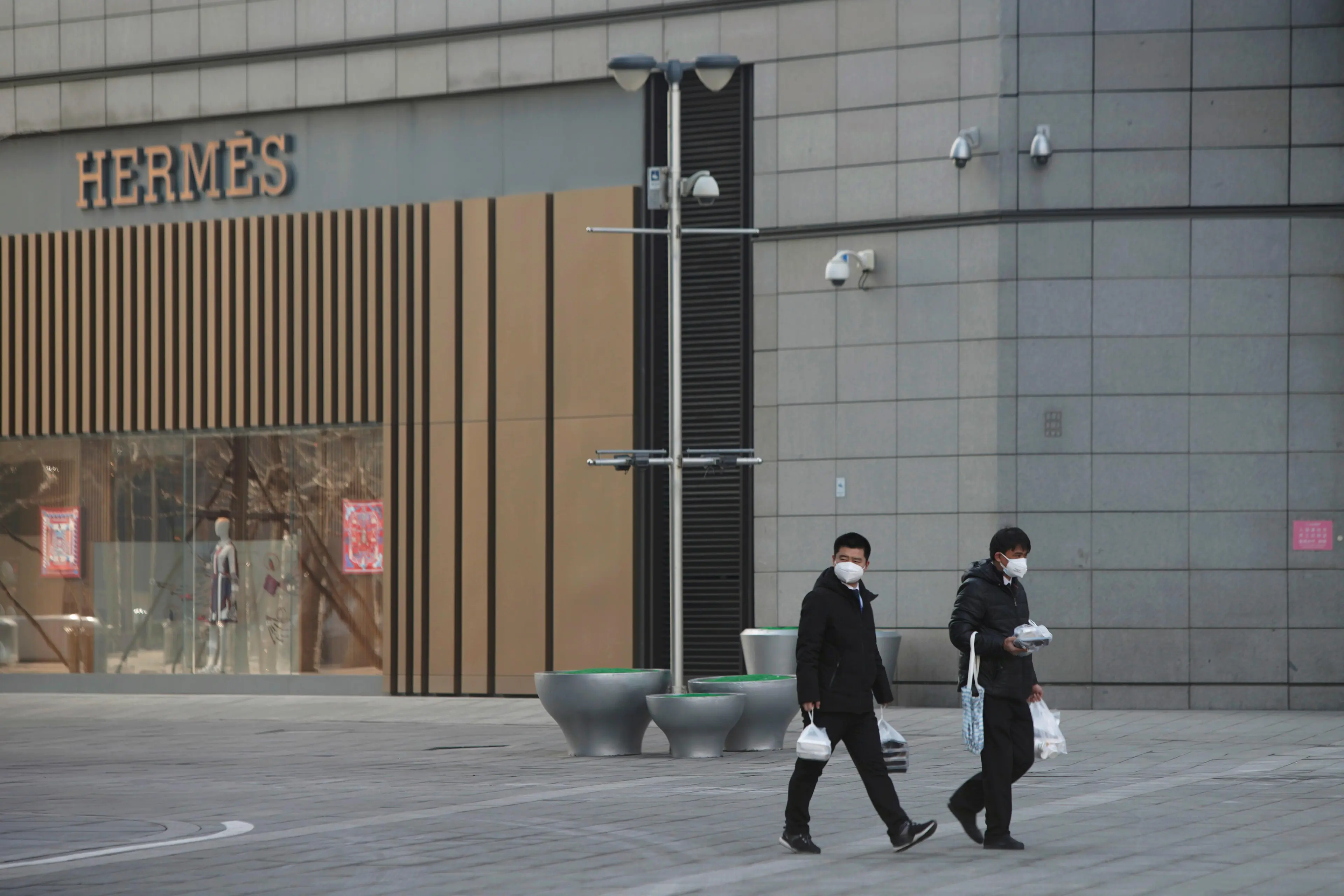 Men wearing face masks walk with takeaway food past a Hermes store at a shopping centre after the extended Lunar New Year holiday caused by the novel coronavirus outbreak, in Beijing\\'s central business district, China February 10, 2020. , Reuters Images/Stringer  