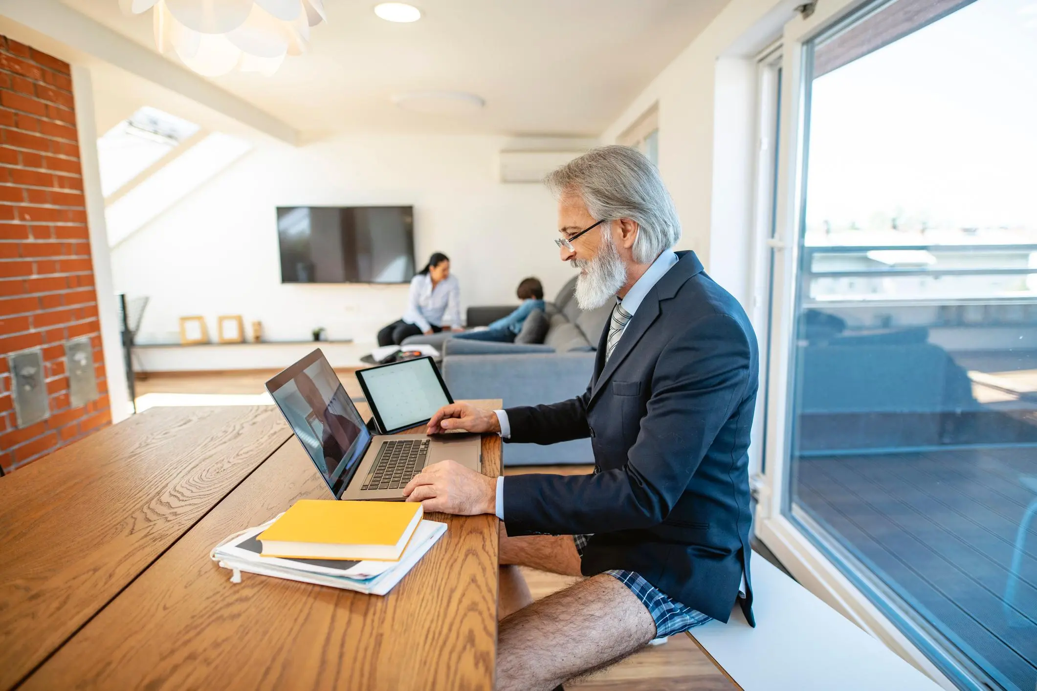 Mature businessman at dining table in front of laptop wearing shirt, tie, suit jacket and boxer shorts as he participates in video call during 2020 quarantine.  , Getty Images/AzmanJaka