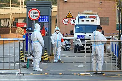Workers in protective suits stand at an entrance to a university\\'s residential area under lockdown following the coronavirus disease (COVID-19) outbreak in Xian, Shaanxi province, China December 20, 2021. Picture taken December 20, 2021. China Daily via REUTERS 